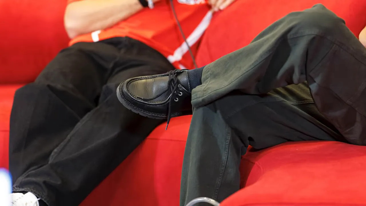 Close-up of black dress shoes worn with dark trousers on a red press conference sofa