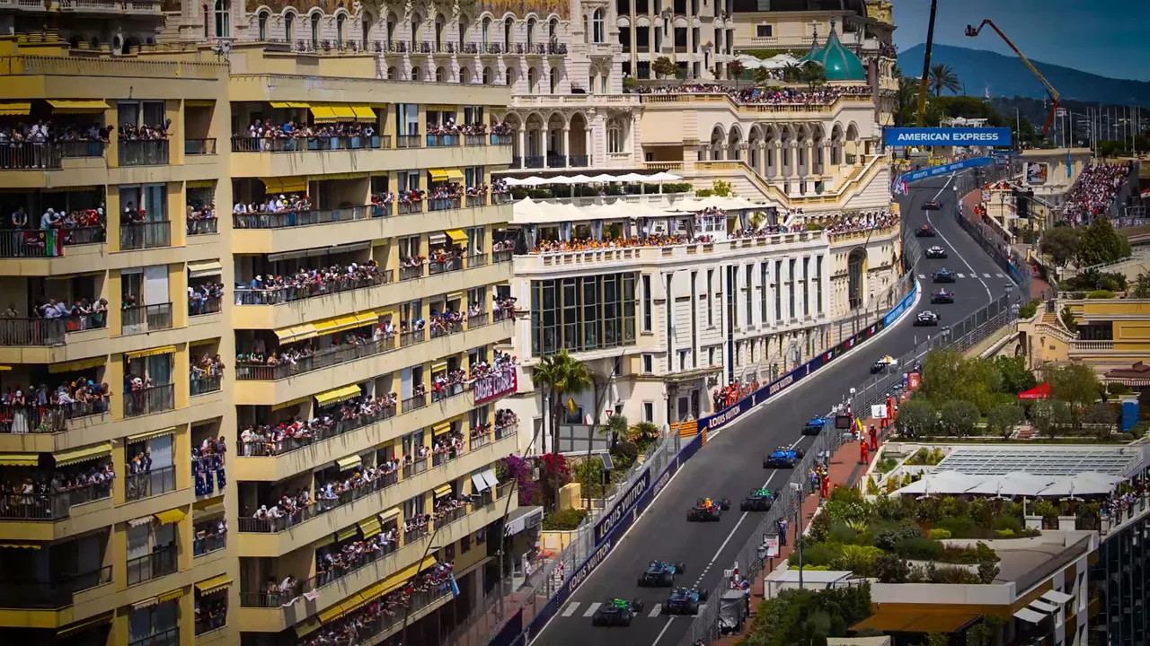 High angle view of Formula 1 cars climbing the hill past Monaco buildings and balconies