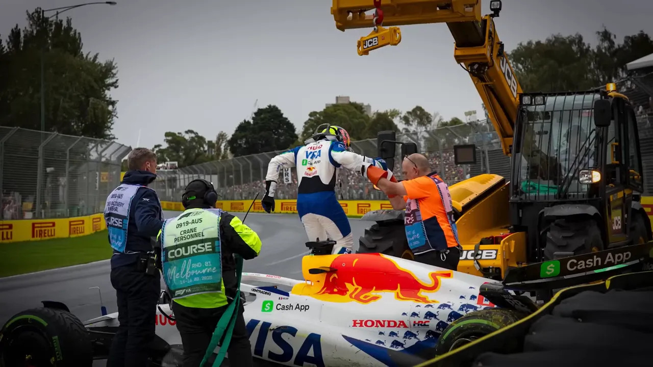 Marshals and recovery crew helping a driver climb from a stricken open-wheel car as a crane prepares to remove it