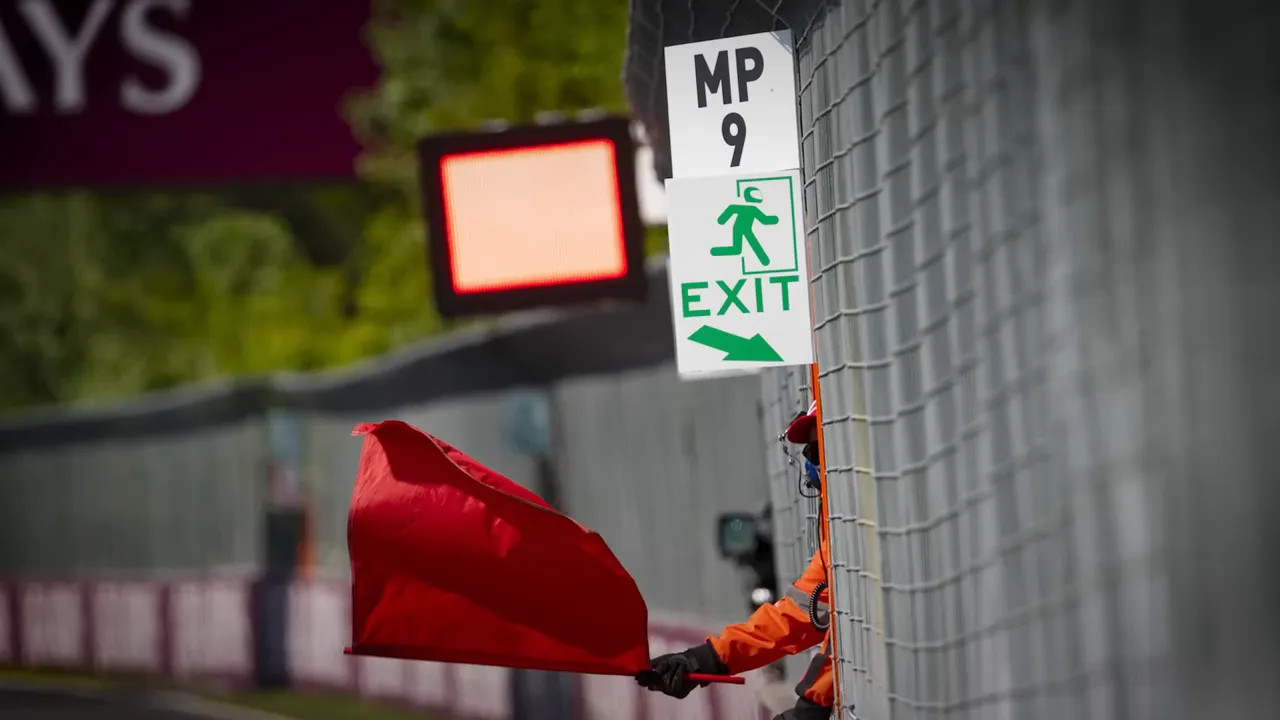 Track marshal waving a red flag beside a safety fence with an illuminated board
