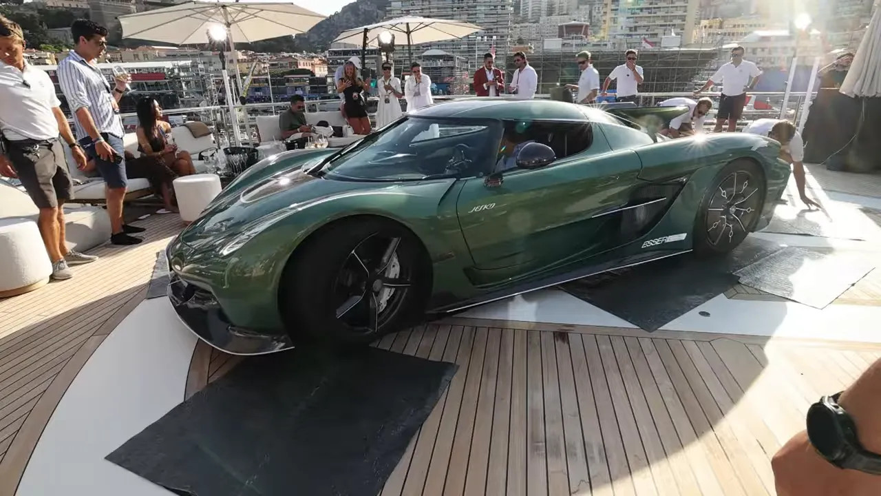 Green hypercar displayed on the yacht deck with guests and yacht structures around it