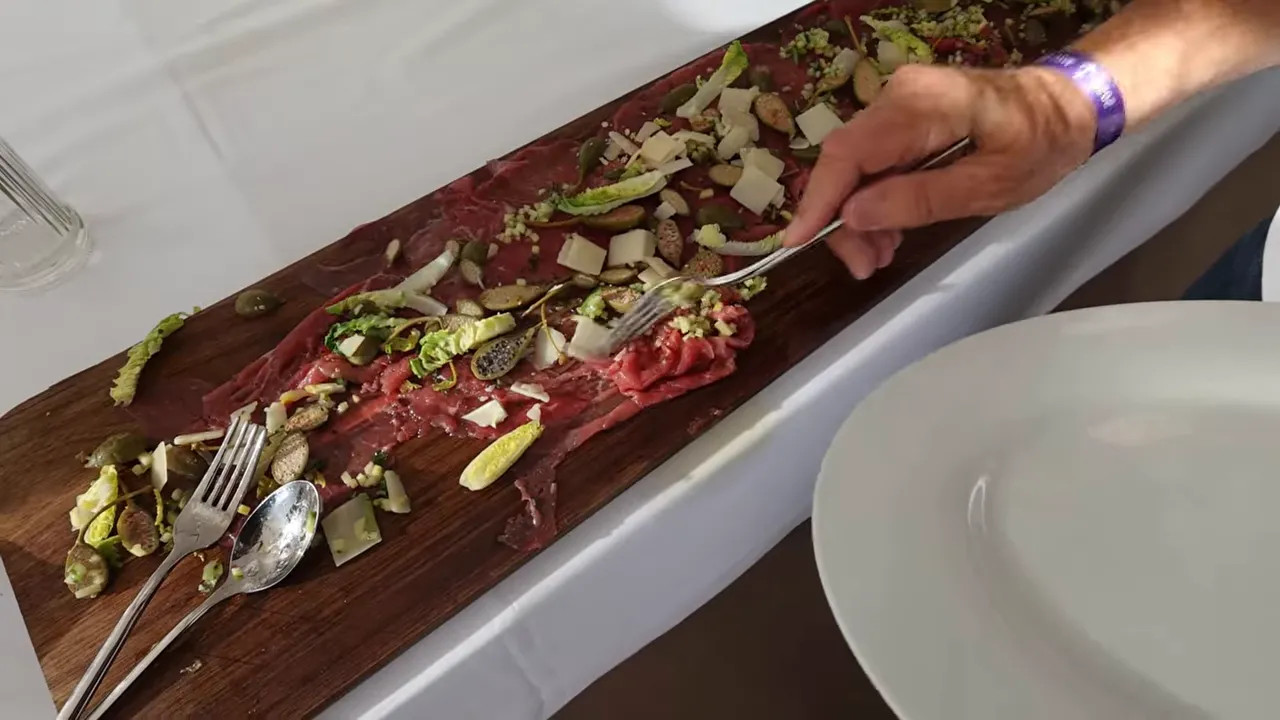 Long platter of beef carpaccio topped with shaved cheese and garnish on a white counter