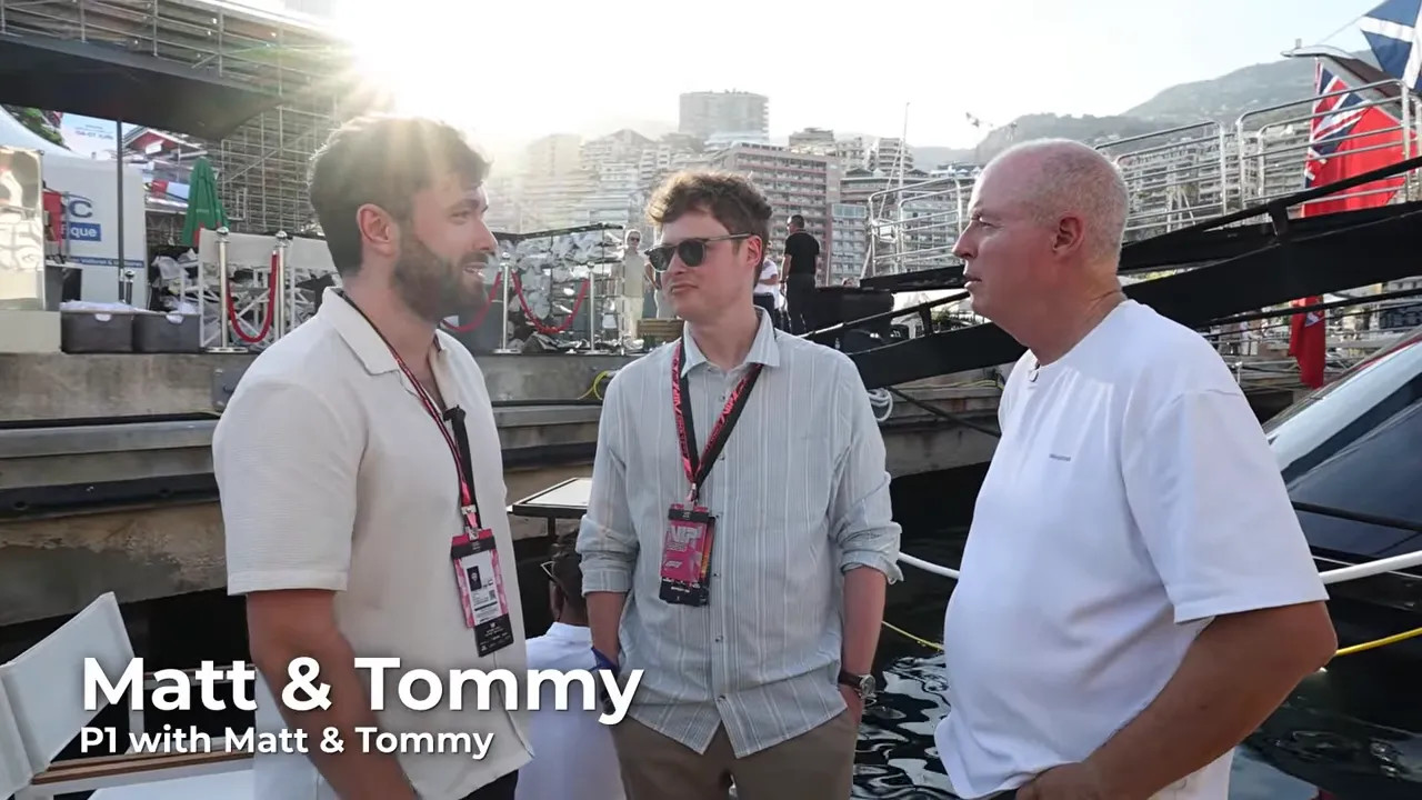 Three men talking beside the yacht with harbour structures and boats in the background
