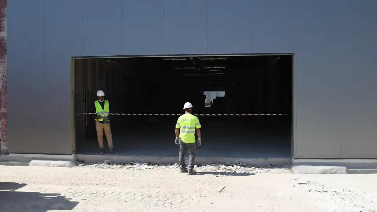 Large garage opening under construction with two workers standing in front