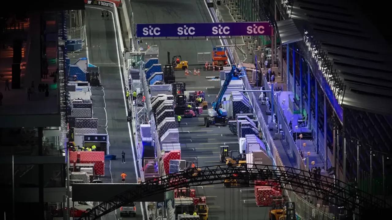 Aerial view of paddock pit lane at night with stacked freight crates, forklifts and crew vehicles