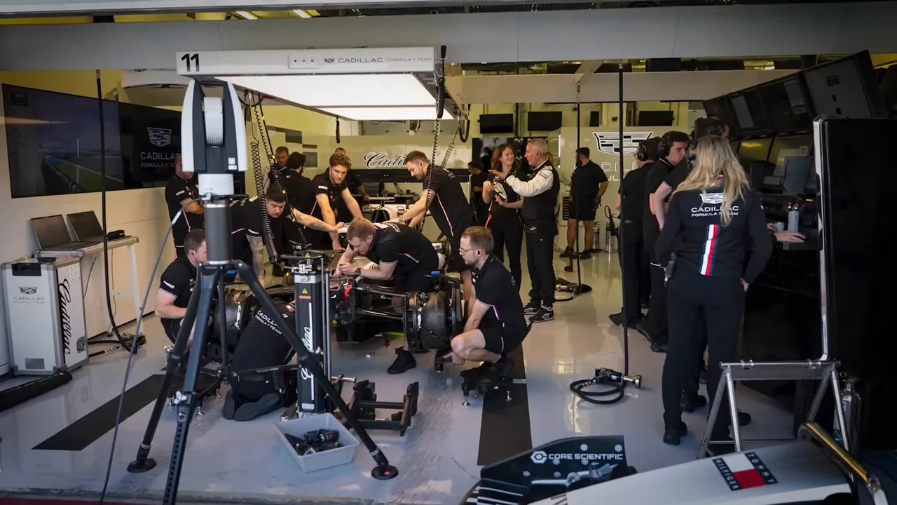 Race mechanics and engineers working on an open-chassis race car inside a busy team garage.