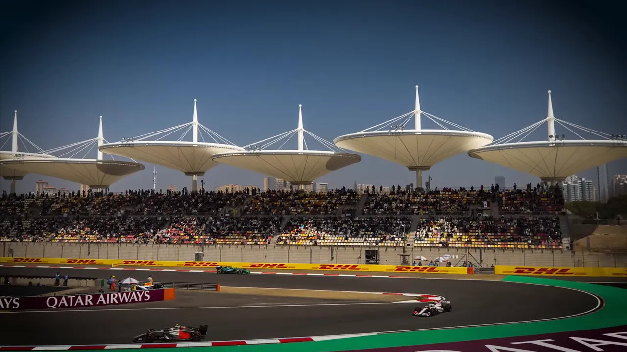 Two Formula 1 cars racing around a track with grandstands and stadium lights